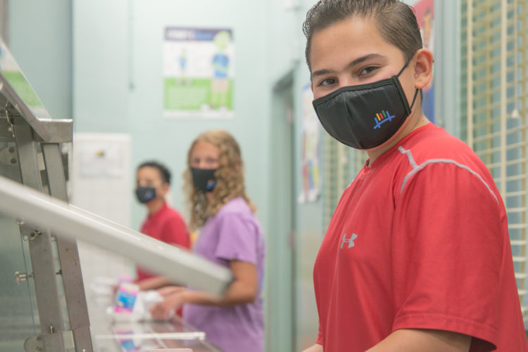 Photo of children with face masks social distancing in a cafeteria line