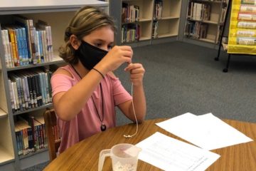 Lone Star elementary student places beads onto bracelet as part of offline coding activity