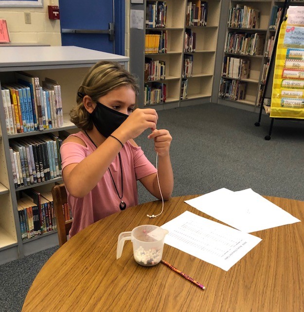 Lone Star elementary student places beads onto bracelet as part of offline coding activity