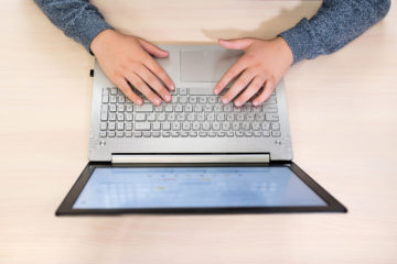 Photo shows overhead shot of hands on laptop keyboard