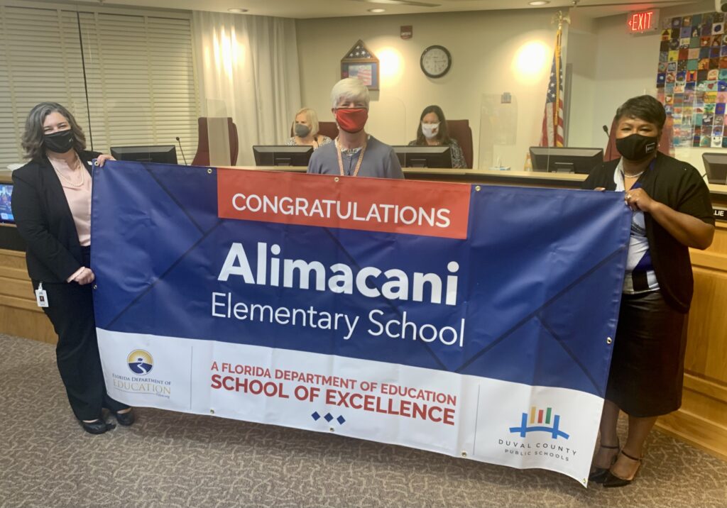 Superintendent, Board Member and school administrator hold banner Congratulations Alimacani Elementary School a Florida Department of Education School of Excellence