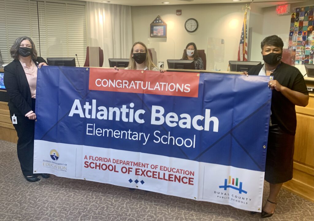 Superintendent, Board Member and school administrator hold banner Congratulations Atlantic Beach Elementary School a Florida Department of Education School of Excellence