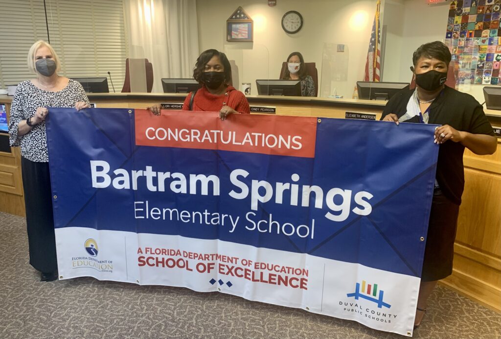 Superintendent, Board Member and school administrator hold banner Congratulations Bartram Springs Elementary School a Florida Department of Education School of Excellence