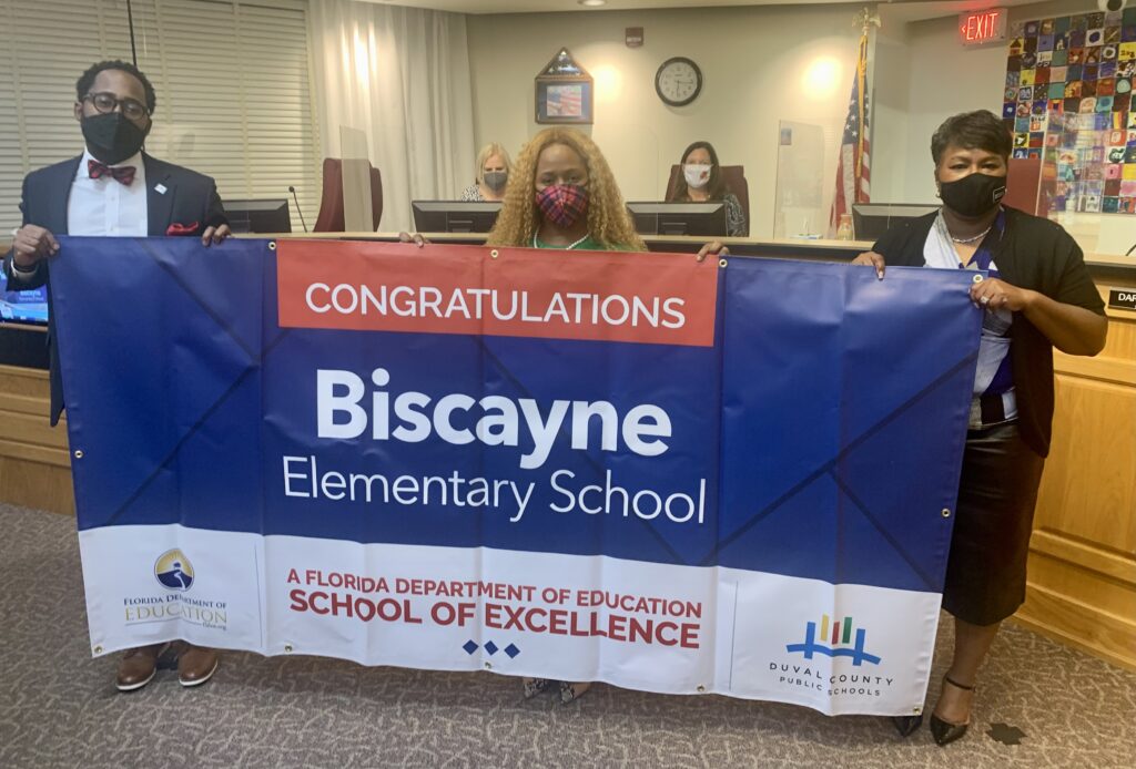 Superintendent, Board Chairman and school administrator hold banner Congratulations Biscayne Elementary School a Florida Department of Education School of Excellence
