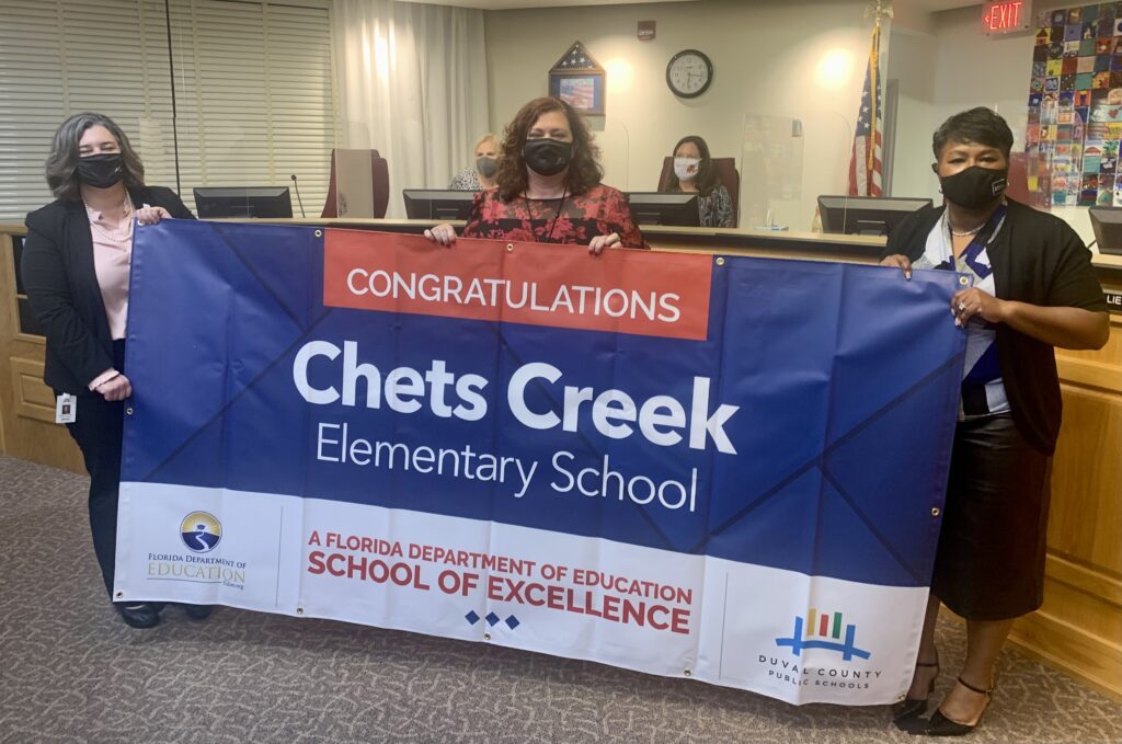 Superintendent, Board Member and school administrator hold banner Congratulations Chets Creek Elementary School a Florida Department of Education School of Excellence