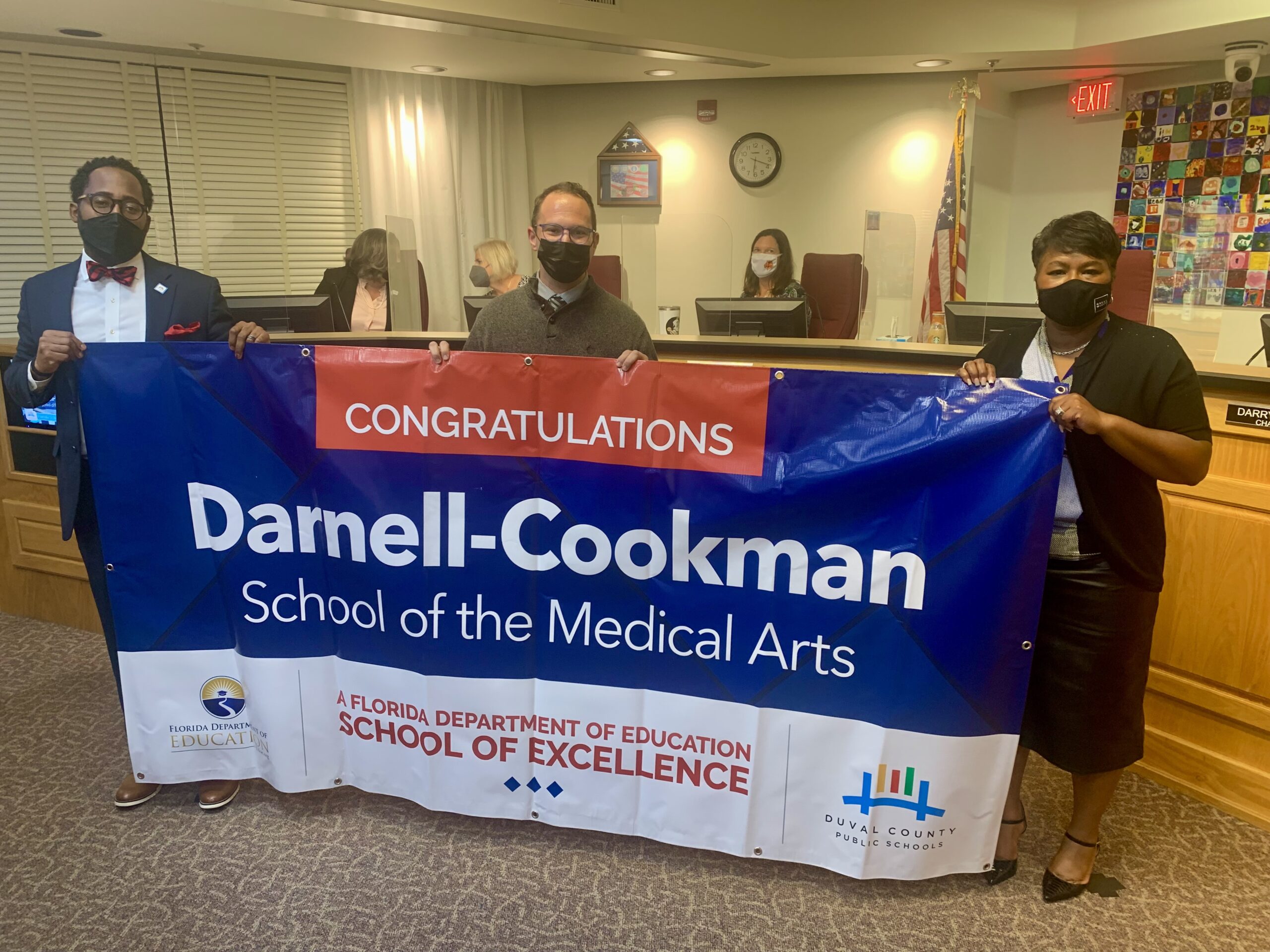 Superintendent, Board Chairman and school administrator hold banner Congratulations Darnell-Cookman School of the Medical Arts a Florida Department of Education School of Excellence