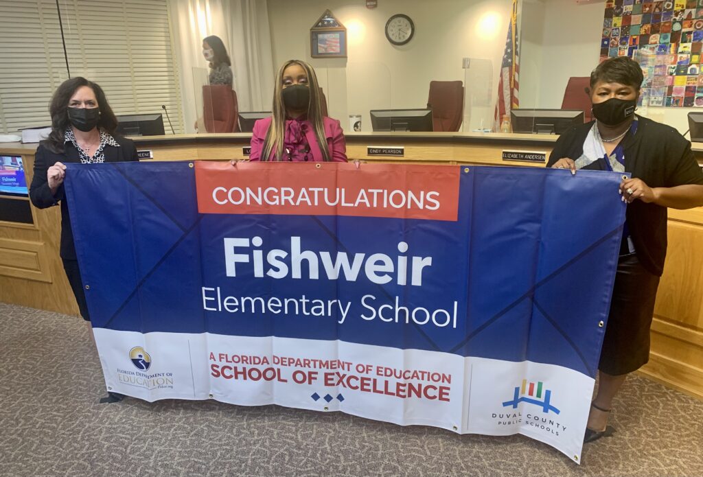 Superintendent, Board Member and school administrator hold banner Congratulations Fishweir Elementary School a Florida Department of Education School of Excellence