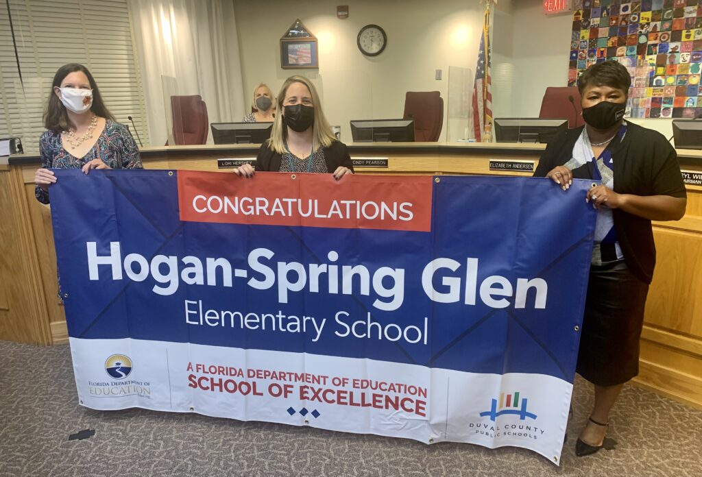 Superintendent, Board Member and school administrator hold banner Congratulations Hogan-Spring Glen Elementary School a Florida Department of Education School of Excellence