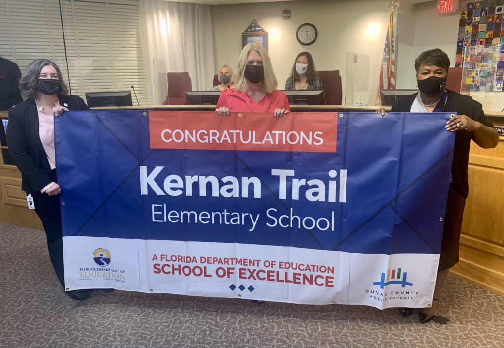 Superintendent, Board Member and school administrator hold banner Congratulations Kernan Trail Elementary School a Florida Department of Education School of Excellence