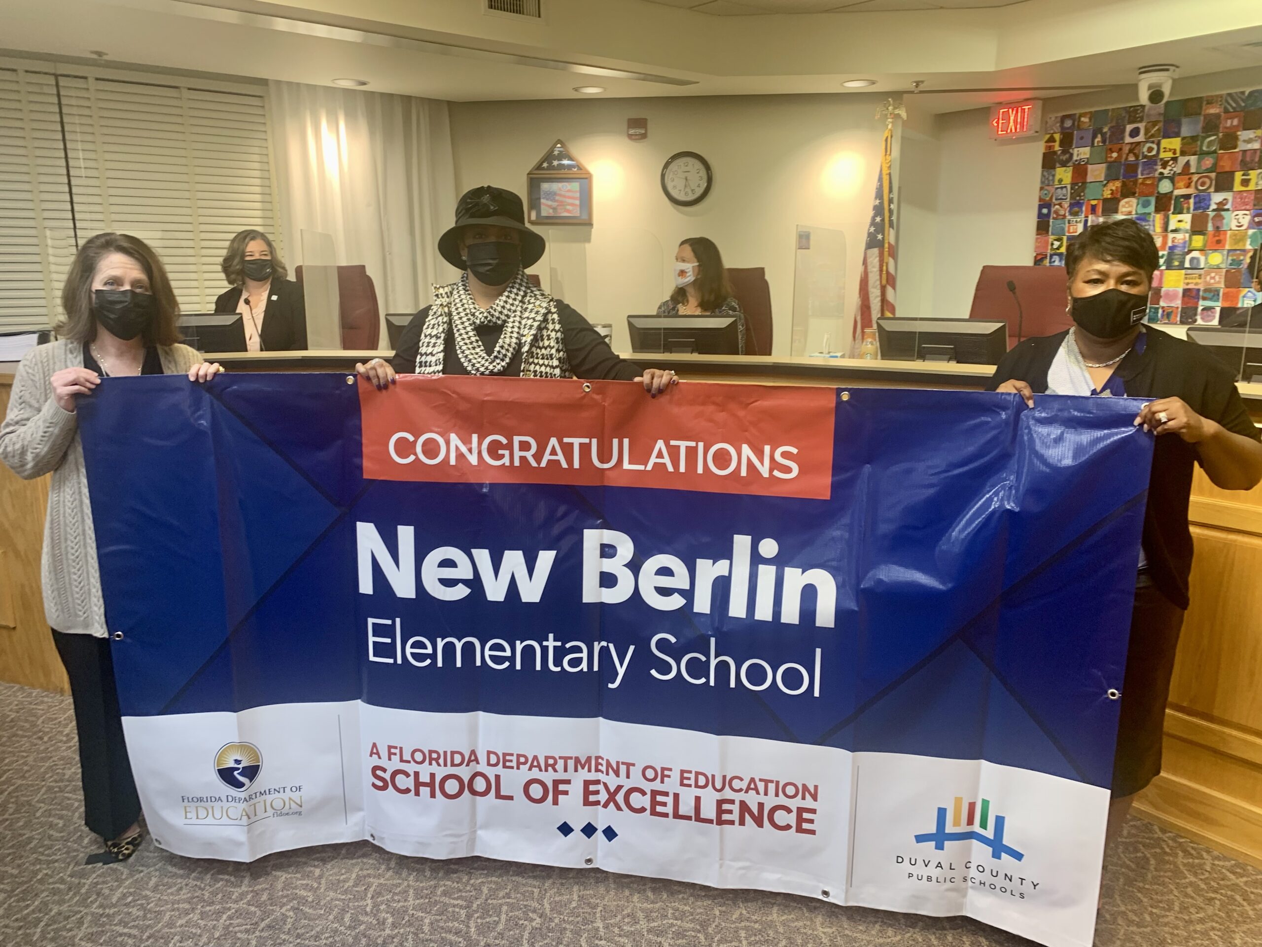 Superintendent, Board Vice-Chairman and school administrator hold banner Congratulations New Berlin Elementary School a Florida Department of Education School of Excellence