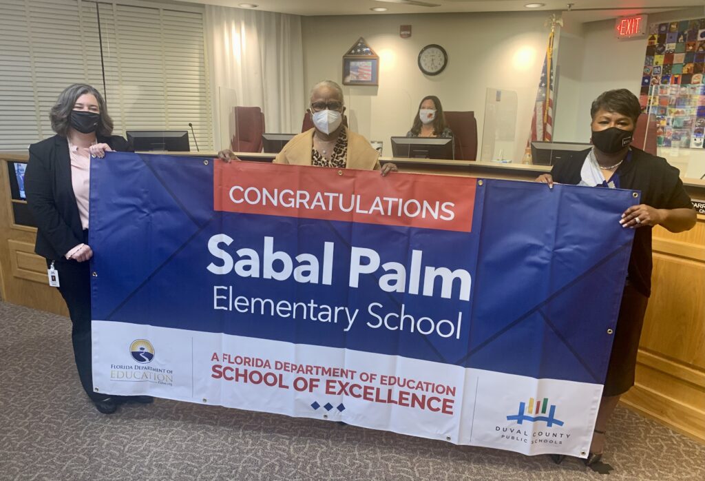 Superintendent, Board Member and school administrator hold banner Congratulations Sabal Palm Elementary School a Florida Department of Education School of Excellence