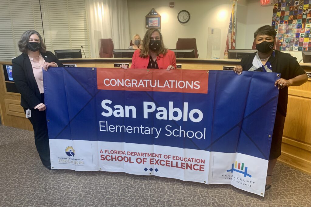 Superintendent, Board Member and school administrator hold banner Congratulations San Pablo Elementary School a Florida Department of Education School of Excellence