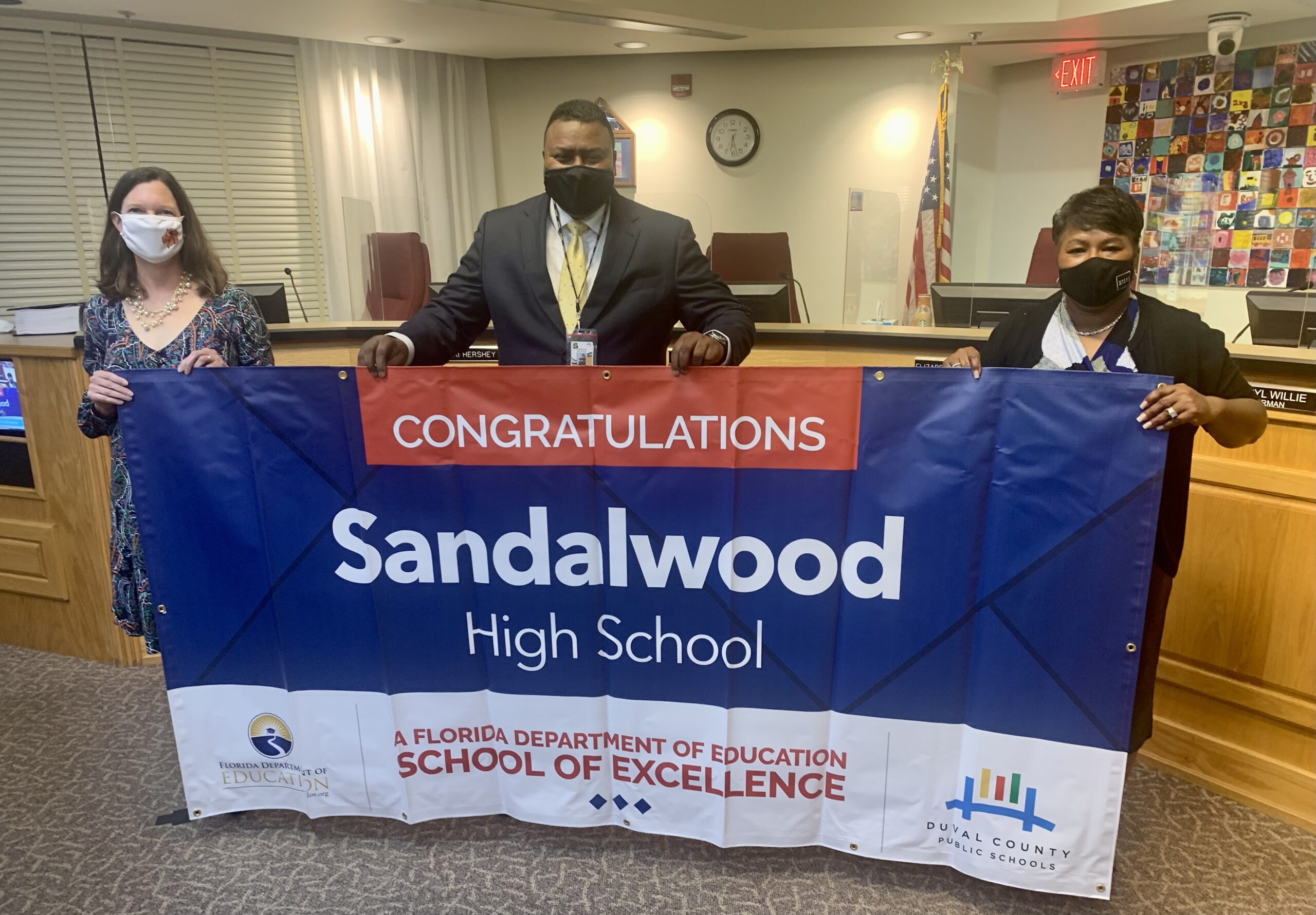 Superintendent, Board Member and school administrator hold banner Congratulations Sandalwood High School a Florida Department of Education School of Excellence