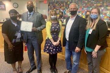 Honoree John Wells stands holding his certificate with Superintendent Dr. Greene and representatives from Embry-Riddle