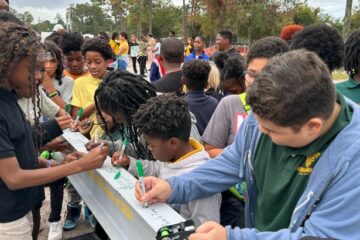 Close up of students signing a silver construction beam.