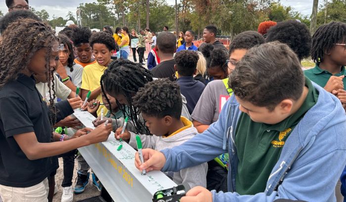 Close up of students signing a silver construction beam.