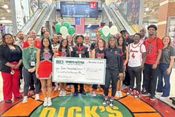 Students and staff pose in the lobby of Dick's Sporting Goods with a large check.