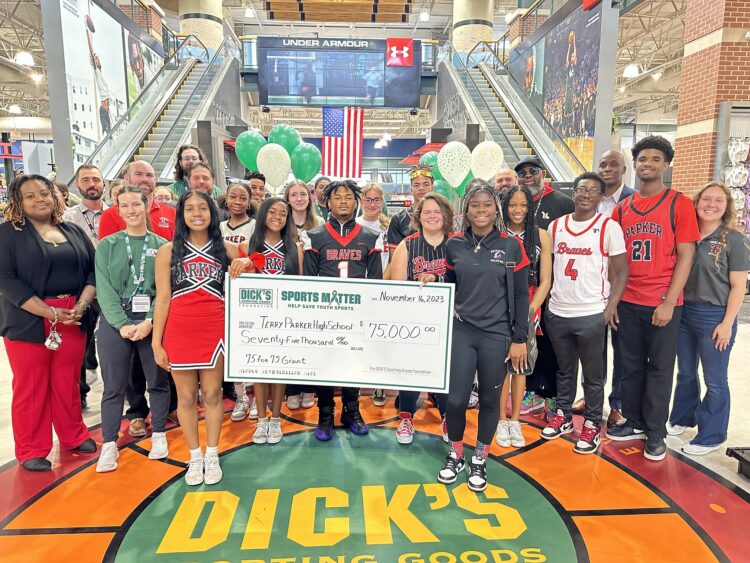 Students and staff pose in the lobby of Dick's Sporting Goods with a large check.