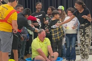 Students pour cups of lemonade onto the school coach as part of their prize for raising the most money.