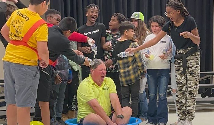 Students pour cups of lemonade onto the school coach as part of their prize for raising the most money.